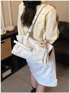 Detail of white glossy tote bag featuring metal buckles and a cute teddy bear charm
