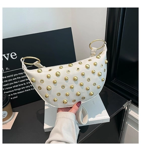 Detail of white half-moon bag with golden studs and metal rivets on shoulder strap