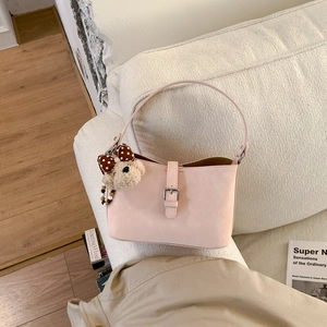 Pink matte leather handbag detail with metal buckle and cute bear charm on sofa