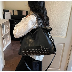 Detail of a black faux leather tote bag with silver rivets and adjustable strap