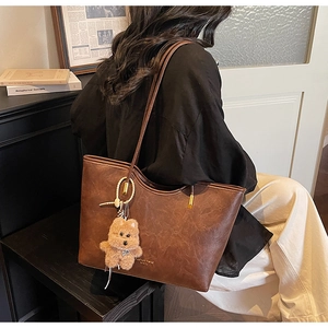 Detail of dark brown tote bag with retro leather texture and cute plush bear charm accessory