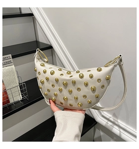 Close-up of white crescent bag with gold stud details and metal ring handle texture