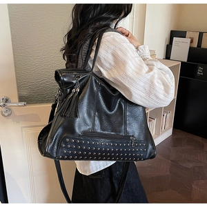 Detail of black tote bag featuring metallic rivets, fringe charm, and long shoulder strap