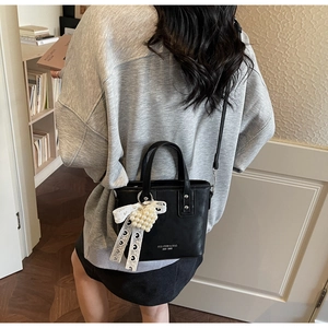 Detail der schwarzen Mini-Beuteltasche mit Perlen- und Bandanhänger an einem Modell