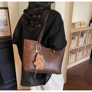 Detail shot of a dark brown faux leather tote bag with a golden hardware and bear charm