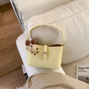 Detail of light yellow underarm bag with a cute plush bear charm on a soft sofa