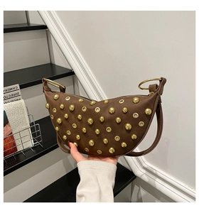 Macro detail of dark brown crescent bag featuring golden studs and metal eyelets