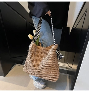Close-up of woven straw tote bag featuring black and white striped knot shoulder straps