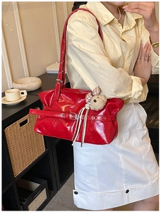Detail of red patent leather shoulder bag with buckle strap and plush bear charm