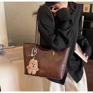 Close-up of brown leather tote bag with wavy edge design and plush bear pendant detail
