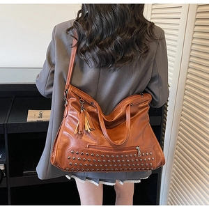 Detailed macro view of the brown retro leather tote bag with metal rivets and fringe tassel