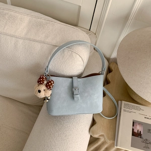 Detail of light blue pleated leather shoulder bag with plush bear charm on white sofa