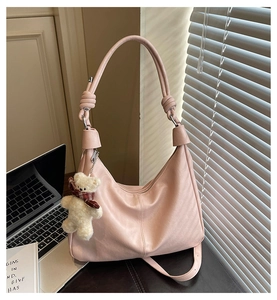 Detailed view of pink hobo tote bag with a plush bear charm on office desk