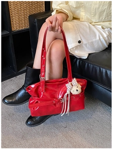 Detail of red patent leather tote bag with buckle strap and plush bear charm