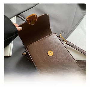 Detail view showing golden magnetic buckle and high-quality leather texture of the brown bag