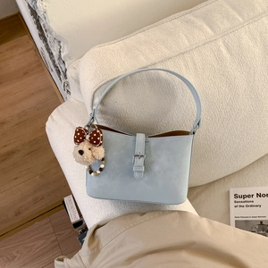 Detail of light blue crossbody bag with silver buckle and plush bear charm on white sofa