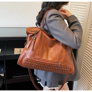 Detail of vintage caramel tote bag featuring metal rivets, tassels and zipped pocket
