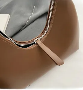 Gros plan sur la fermeture éclair argentée et la tirette en cuir marron du sac