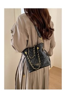 Détail du sac seau noir matelassé avec chaîne dorée et logo de marque sur le cuir