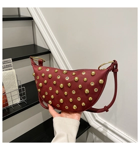 Detail of red crescent shoulder bag featuring gold studs and metal ring handle