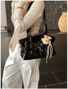 Detail of glossy black tote bag with silver buckles and a cute plush bear pendant accessory