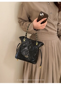 Détail du sac seau noir matelassé avec bandoulière chaîne dorée et nom de marque