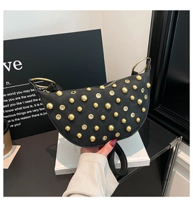 Close-up of black crescent bag featuring gold stud rivets and a circular metal handle