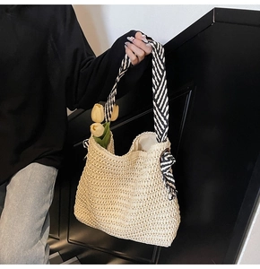 Detail view of woven straw tote bag featuring black and white striped shoulder straps