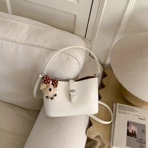 Detail of cream bucket bag with faux leather texture and cute teddy bear charm