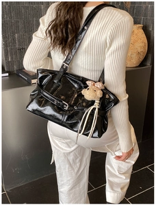 Detail of glossy black patent leather tote with metal buckle and plush sheep charm