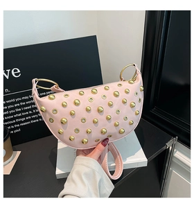 Pink crescent underarm bag with gold metallic studs and eyelets shown in hand