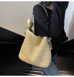 Detail of handwoven straw tote bag with black and white striped fabric shoulder strap