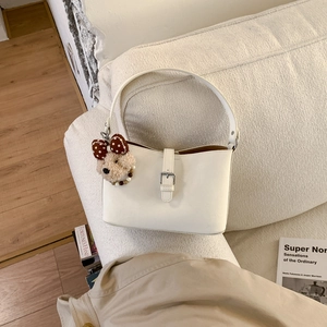 Detail of creamy white PU leather shoulder bag with buckle and plush bear pendant