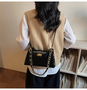 Detail of glossy black patent leather shoulder bag with gold chain and metal turn-lock