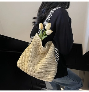 Close-up of beige straw woven tote bag with stylish black and white striped wide strap