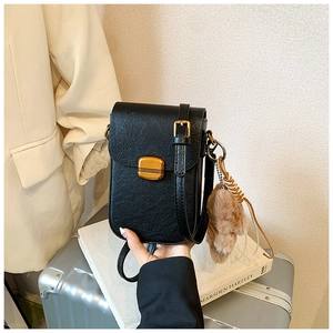 Detail of black crossbody phone bag with bronze buckle and brown plush bear charm