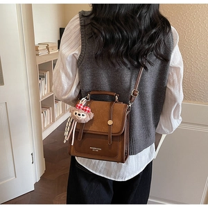 Close-up of retro brown PU leather backpack with teddy bear charm in a cozy library setting