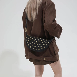Detail of black half-moon crossbody bag with gold rivets worn on model's shoulder