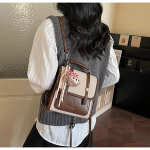 Detail of vintage contrast color leather backpack featuring metal buttons and a plush charm
