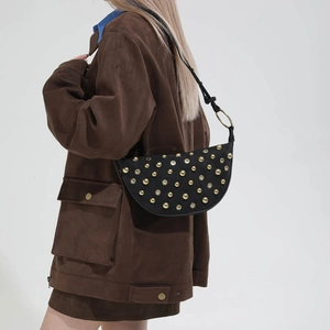 Detail of black leather half-moon bag with gold eyelet studs and metallic ring strap