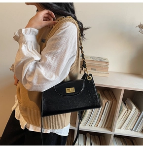 Détail du sac bandoulière en cuir verni noir avec chaîne dorée et fermoir pivotant
