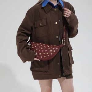 Detail of burgundy half-moon bag with golden studs and metal eyelets on leather