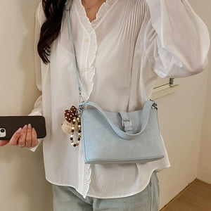 Close-up of light blue textured leather crossbody bag with silver buckle and plush charm