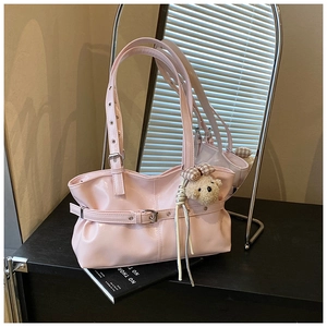 Detail of glossy pink underarm bag featuring a decorative belt buckle and plush bear charm