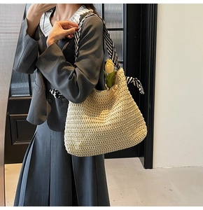 Detail of handwoven straw tote bag with stylish black and white striped shoulder strap