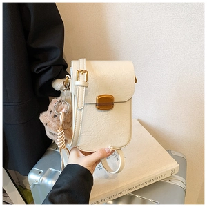 Detail view of cream vertical crossbody bag with golden square lock and teddy bear charm