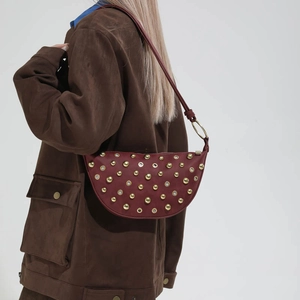 Detail of burgundy crescent shoulder bag with golden studs and metal eyelets on model