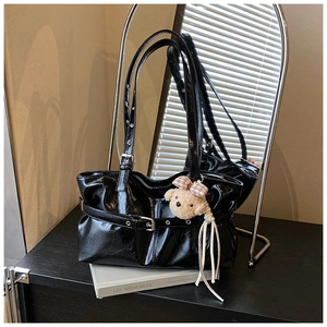 Detail of glossy black patent leather tote bag with silver buckle and plush bear charm