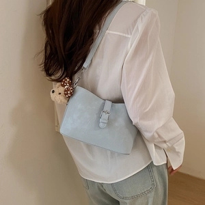 Close-up of light blue textured leather shoulder bag with a cute brown teddy bear charm