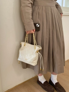 Détail du cuir ivoire matelassé et du logo doré sur un sac seau élégant